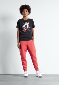 Schwarzes T-Shirt mit rographic und weißer Grafik, kombiniert mit korallenfarbigen Jogginghosen und weißen Sneakers. Das Outfit zeichnet sich durch bequeme, lässige Stile aus.