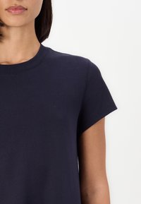 Granatowa bawełniana koszulka z okrągłym dekoltem i krótkimi rękawami. Posiada gładką fakturę i luźny krój. Minimalistyczny design i detale.