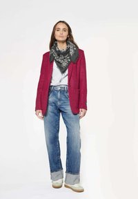 Rode getextureerde blazer over een gestreepte shirt, met blauwe denim jeans met opgerolde zoom en witte sneakers. Zwarte geprinte sjaal voegt detail toe.