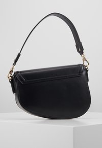 Svart läderhandväska med en böjd form, justerbar axelrem och guldackenter. Har en klaffstängning och en slät yta.