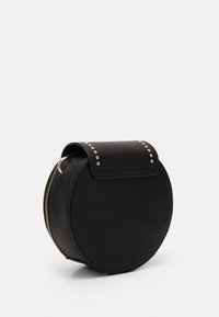 Runde schwarze Ledertasche mit Reißverschluss, strukturierter Oberfläche, Nietenakzenten auf der Klappe und einem oberen Griff zum Tragen.