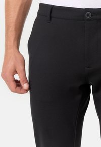 Crne muške tapered hla�če izrađene od glatkog materijala, s prednjim kopčanjem na dugme, petljama za pojas i bočnim džepovima.