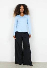 Cămașă cu mânecă lungă bleu deschis și decolteu cu margini ondulate, asortată cu pantaloni negri cu croială largă. Material neted și croială lejeră.