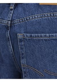 Primo piano di jeans in denim blu che mostrano la tasca posteriore, i dettagli delle cuciture e la trama del tessuto.