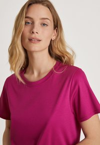 Magenta t-shirt van soepele stof, met een ronde halslijn en korte mouwen. Het materiaal lijkt lichtgewicht met een subtiele glans.