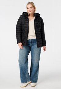 Zwarte gewatteerde jas met een capuchon, ritssluiting aan de voorkant en ribbelstructuur. Gepaard met lichtblauwe wijde jeans en witte sneakers.