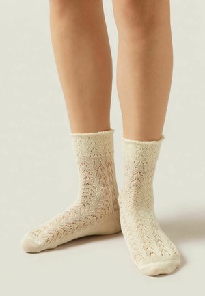 Chaussettes crème montantes ornées d'un motif en dentelle, avec un bord froncé et un design texturé, fabriquées en matiere tricot légère.