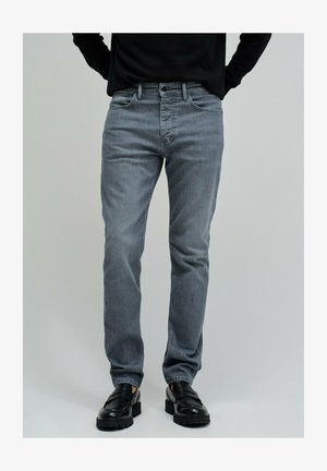 Grijze denim jeans met een slanke pasvorm, voorzien van een klassieke vijfzakkenontwerp, subtiele vervaging en metalen details. Gecombineerd met zwarte schoenen.