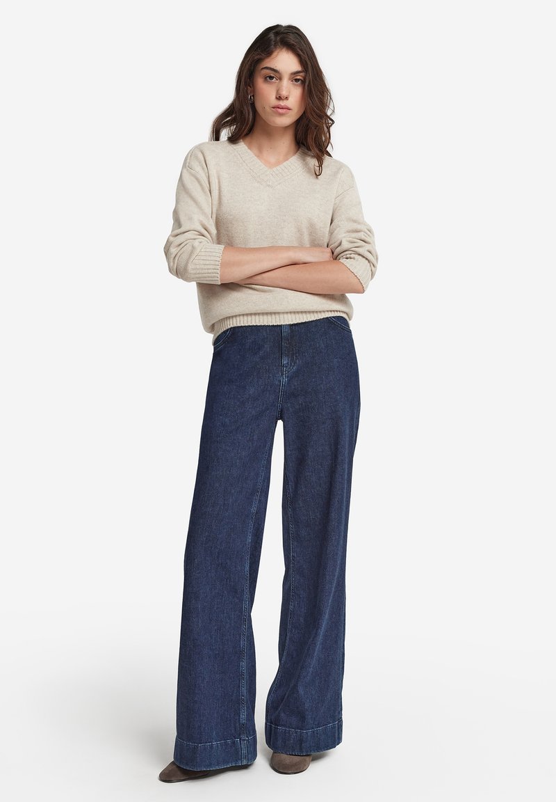 Beige v-ringad tröja med ribbad manschett, i kombination med högmidjade, vida mörkblå denimjeans med fållad nederkant.