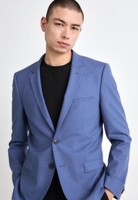 Sacou bleu deschis cu rever în formă de notch, închidere cu un singur nasture și două buzunare frontale. Purtați peste o cămașă neagră cu o textură netedă.