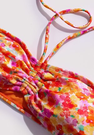 Tissu fleuri coloré avec des fronces et des fines bretelles, conçu pour un maillot de bain ou un haut d'été sur fond blanc.