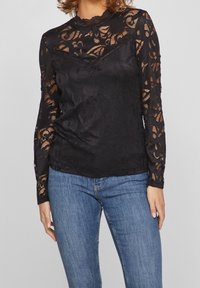 Sort blonde langærmet top med blomsterprint, bølget halsudskæring og tætsiddende silhuet, kombineret med blå denim jeans.