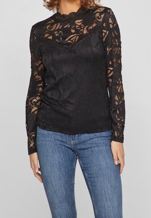 Black lace long-sleeve top with floral pattern, scalloped neckline, and fitted silhouette, paired with blue denim jeans.