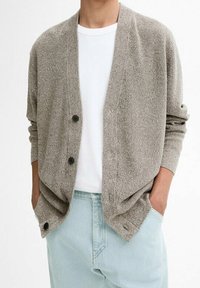 Grå stickad kofta med en avslappnad passform, med en sjalkrage, framknappar och sidofickor, kombinerad med en vit t-shirt och ljusblå jeans.