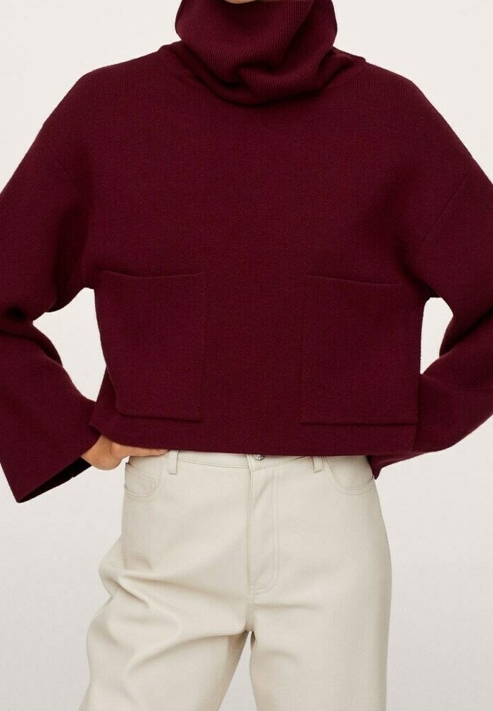 Burgunderfarbener Strickrollkragenpullover mit weit geschnittenen Ärmeln und zwei vorderen Taschen, der eine weiche Textur und ein kurzes Design aufweist. Kombiniert mit cremefarbenen Hosen.