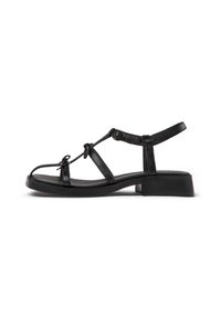 Black sandal with a block heel, featuring thin straps, ankle support, and knotted accents. Smooth texture on the upper and sole.