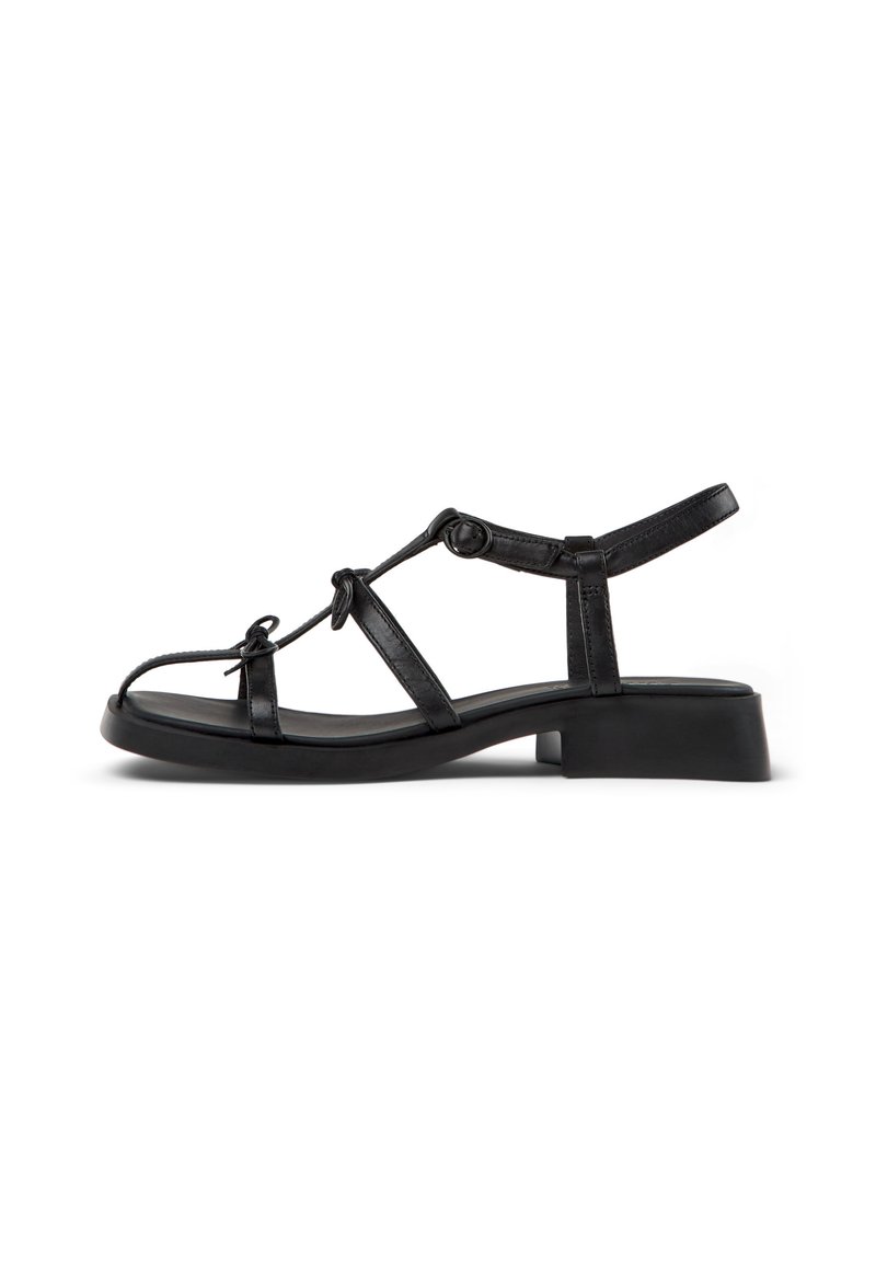 Black sandal with a block heel, featuring thin straps, ankle support, and knotted accents. Smooth texture on the upper and sole.