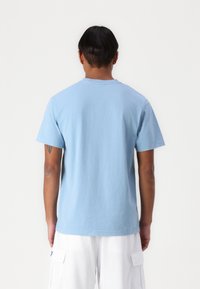 Light blue cotton t-shirt with short sleeves, standard crew neck, and a smooth texture, displayed from the back. White cargo shorts visible.