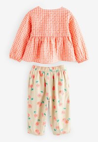 Top peplum in stampa a scacchi arancione, abbinato a pantaloni beige con stampa floreale rosa e gambi verdi. Pantaloni con vita elastica.