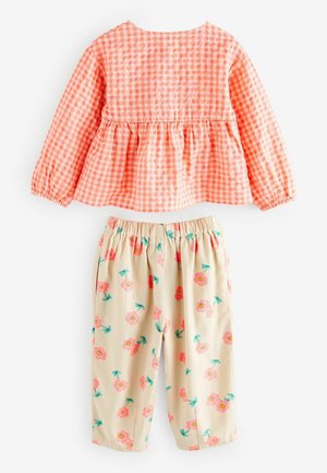 Top peplum in stampa a scacchi arancione, abbinato a pantaloni beige con stampa floreale rosa e gambi verdi. Pantaloni con vita elastica.
