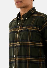 Groen geruite button-up shirt met gele en marineblauwe strepen. Heeft een puntige kraag en een voorzak, gemaakt van zachte, gestructureerde stof.