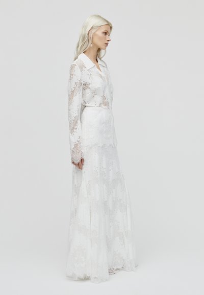 Witte kanten jurk met lange mouwen, voorzien van een puntige kraag en een gelaagd rokdesign, met intrigerende bloemmotieven.