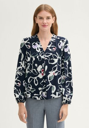 Blouse marine à motif floral en blanc, vert et rouge. Présente un col en V et de longues manches froncées. Tissu léger avec une texture lisse.