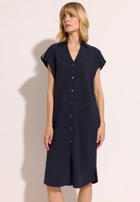 Granatowa sukienka z krótkimi podwiniętymi rękawami, dekoltem w serek oraz bocznymi rozcięciami. Wykonana z gładkiego materiału o luźnym kroju.