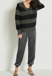 Pull rayé noir et vert foncé avec un col en V et une bordure en dentelle, associé à un pantalon en satin gris se rétrécissant à la cheville. Talons aiguilles noirs avec lanières.