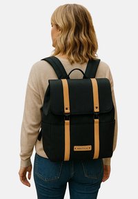 Mochila de tela negra con correas de cuero marr�ón, cierre de solapa, bolsillo frontal y etiqueta de marca. Correas de hombro anchas para una comodidad en el transporte.