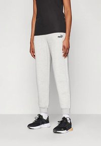 Szare spodnie dresowe ze ściągaczami przy kostkach, wykonane z miękkiego materiału. Na udzie znajduje się subtelne logo Puma. Czarne buty sportowe z żółtymi akcentami.