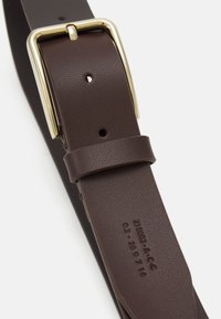 Bruine leren riem met een gouden metalen gesp, voorzien van verschillende verstelgaatjes en reliëfdetails op de band.