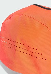 Casquette de sport orange avec une surface texturée et des rayures horizontales, présentant une rangée de petites perforations sur un côté. Accents noirs visibles.