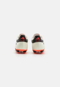 Botas de fútbol blancas con acentos negros y detalles rojos. Presentan una parte superior de cuero liso y una suela texturizada con tacos rojos.