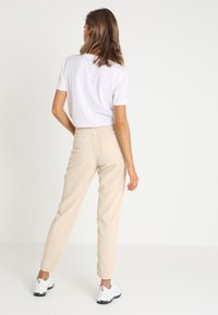 Beiga kordfläckade byxor med en avsmalnande passform, med bakfickor, tillsammans med en vit t-shirt med kort ärm och vita sneakers.