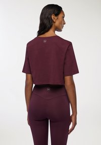 Burgundowy crop top z krótkimi rękawami i okrągłym dekoltem, zestawiony z legginsami o wysokim stanie w pasującym kolorze, z logo na pasku.