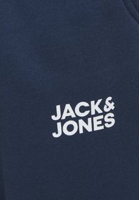 Tessuto blu navy con una superficie liscia, caratterizzato da un logo bianco "JACK & JONES" stampato in modo prominente. Nessun pattern o accessorio aggiuntivo visibile.