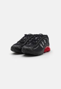 Black athletic shoes with mesh upper, reflective accents, and distinctive red and black sole. Features laces and cushioned heel.