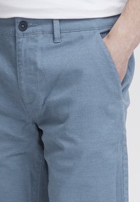 Light blue patterned pants made of textured fabric, featuring front pockets and a single black button closure at the waist.