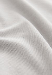 Valkoinen puuvillakangas, jossa on sileä ja pehmeä pinta, hieno ribbikuviointi ja himmeä kiilto, laskeutuen laskoksina.