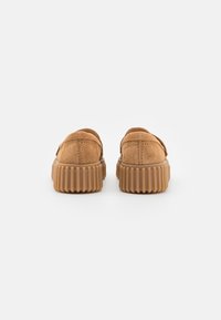 Zapatos de ante marrón con forma redondeada, que cuentan con una suela de goma estriada. El diseño incluye costuras visibles en la parte superior.