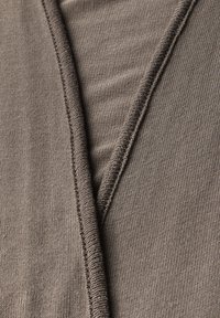Tessuto in maglia marrone con una superficie testurizzata, caratterizzato da un design sovrapposto e cuciture visibili lungo i bordi.