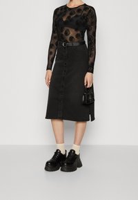 Svart genomskinlig långärmad topp med rosmönster; högmidjad svart jeanskjol med framknappar; kraftiga svarta skor; liten svart handväska.