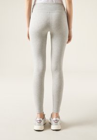 Grå leggings med hög midja, slät textur och en snug passform, iförda med silverfärgade träningsskor, visade bakifrån.