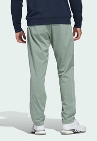 Light green athletic pants with a textured pattern, tapered fit, side pockets, and elastic waistband, paired with white golf shoes.