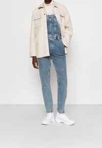 Kerman takki vaaleanbeige poolopaidan päällä, yhdistettynä sinisiin farkkutakkeihin ja valkoisiin tennareihin. Yksinkertainen muotoilu, rento istuvuus.