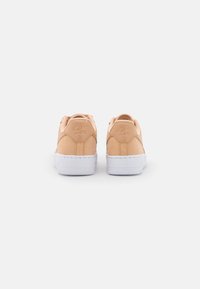 Ljusbeige Nike-sneakers med en slät läderfinish, vita gummisulor och prägling av logotypdetaljen på hälen. Klassisk låg sko-design.