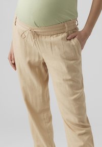 Pantalon en lin beige avec une taille élastique à cordon, des poches latérales et une coupe confortable. Le tissu présente une apparence douce et légèrement texturée.