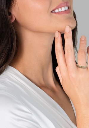 Silberner Ring mit graviertem geometrischem Muster, das an einem Finger getragen wird, mit einer glatten, polierten Oberfläche, vor einem hellen Hintergrund.