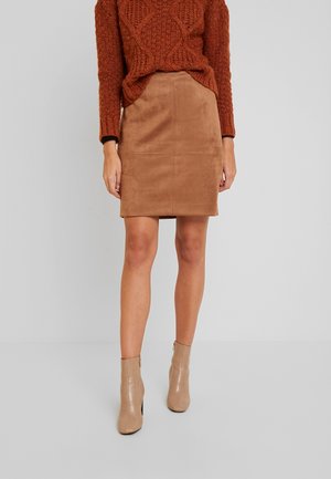 Brauner Wildleder-Minirock mit vorderem Nahtdetail, kombiniert mit beigen Ankle-Boots. Der Strickpullover hat ein strukturiertes Muster in rostfarbener Farbe.